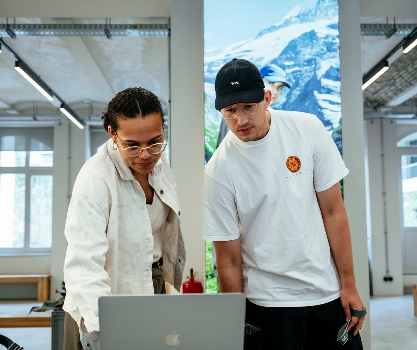 A woman and man standing whilst both looking at a laptop.