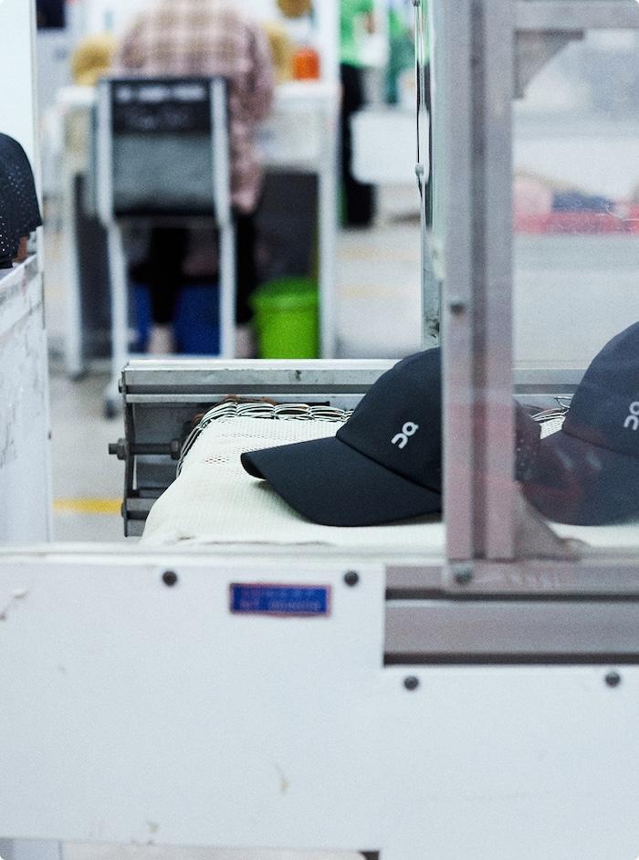 Black caps with a white logo sit on a conveyor belt in a production facility.