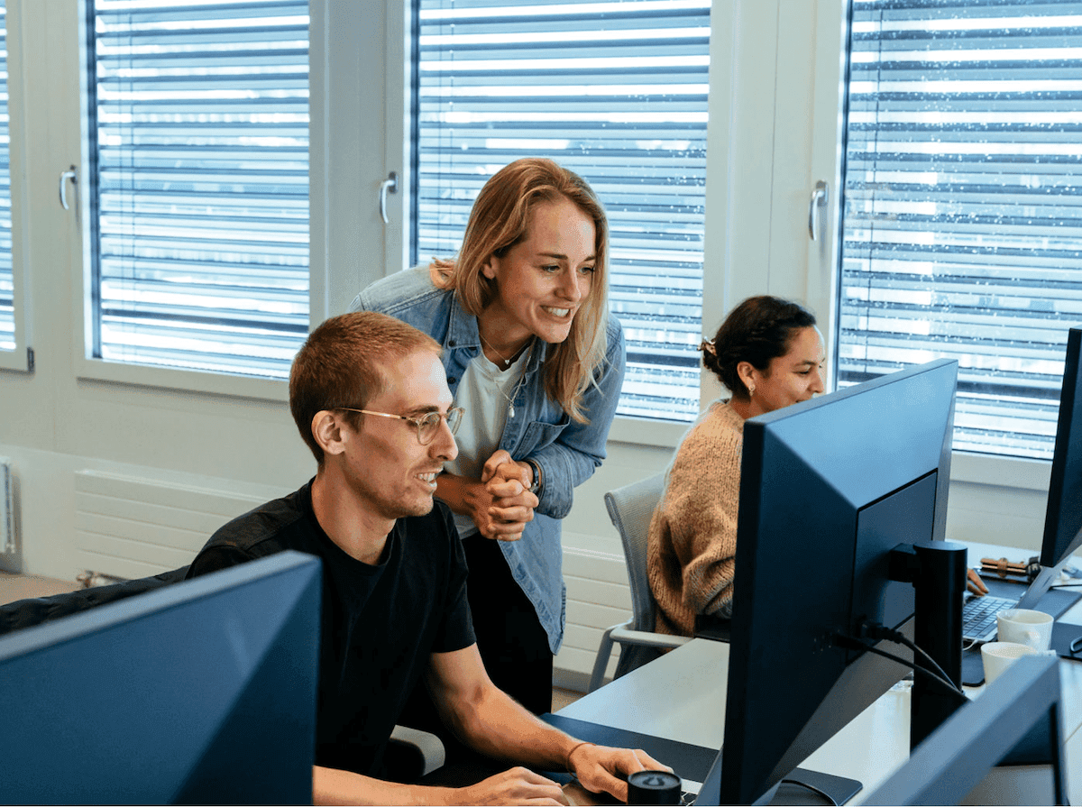A lady overlooking a man working on a computer