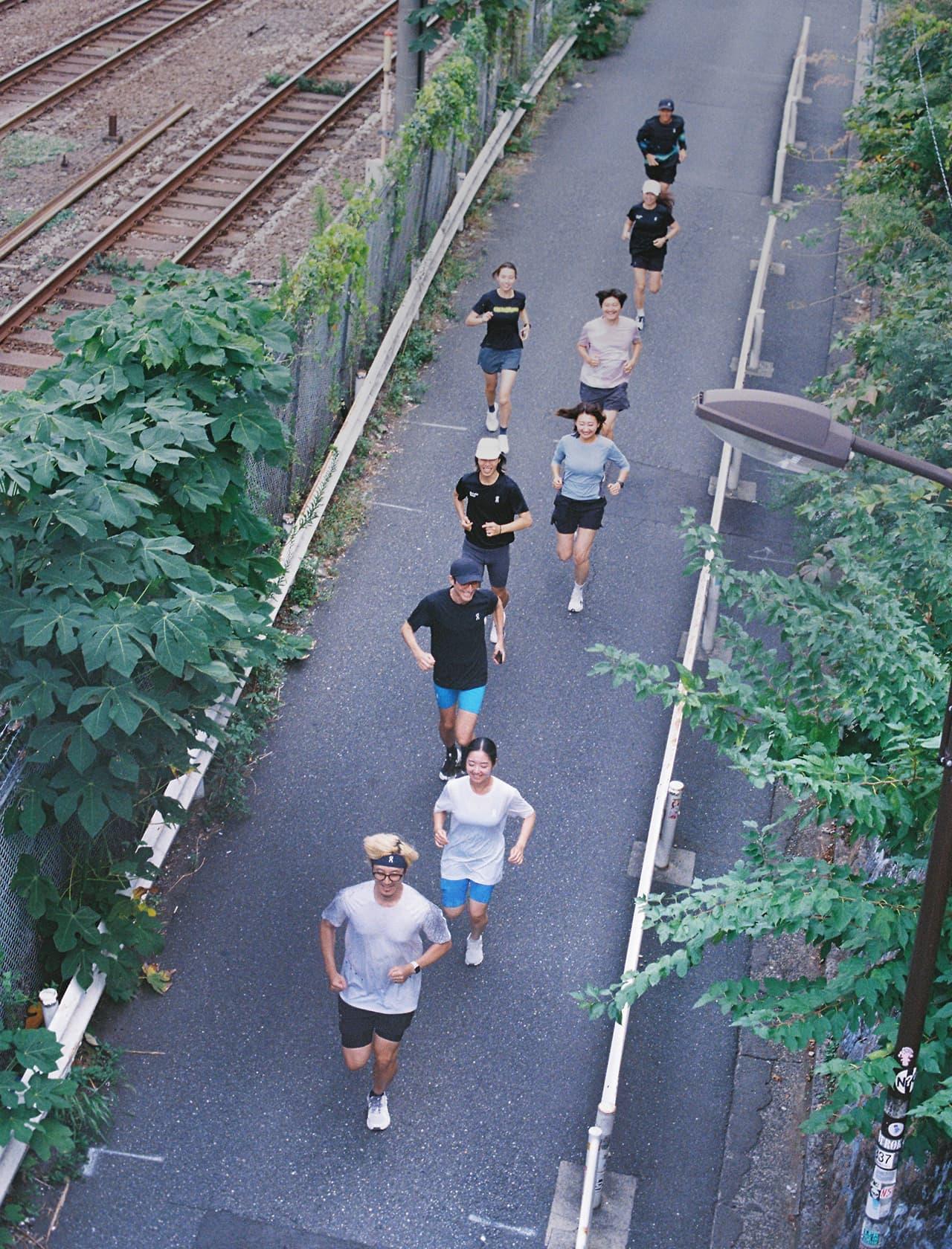 A group of people jogging along a tree-lined paved path beside railroad tracks.