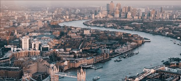 Aerial view of the River Thames winding through London with Tower Bridge in the foreground and the Canary Wharf cluster of skyscrapers in the distance.