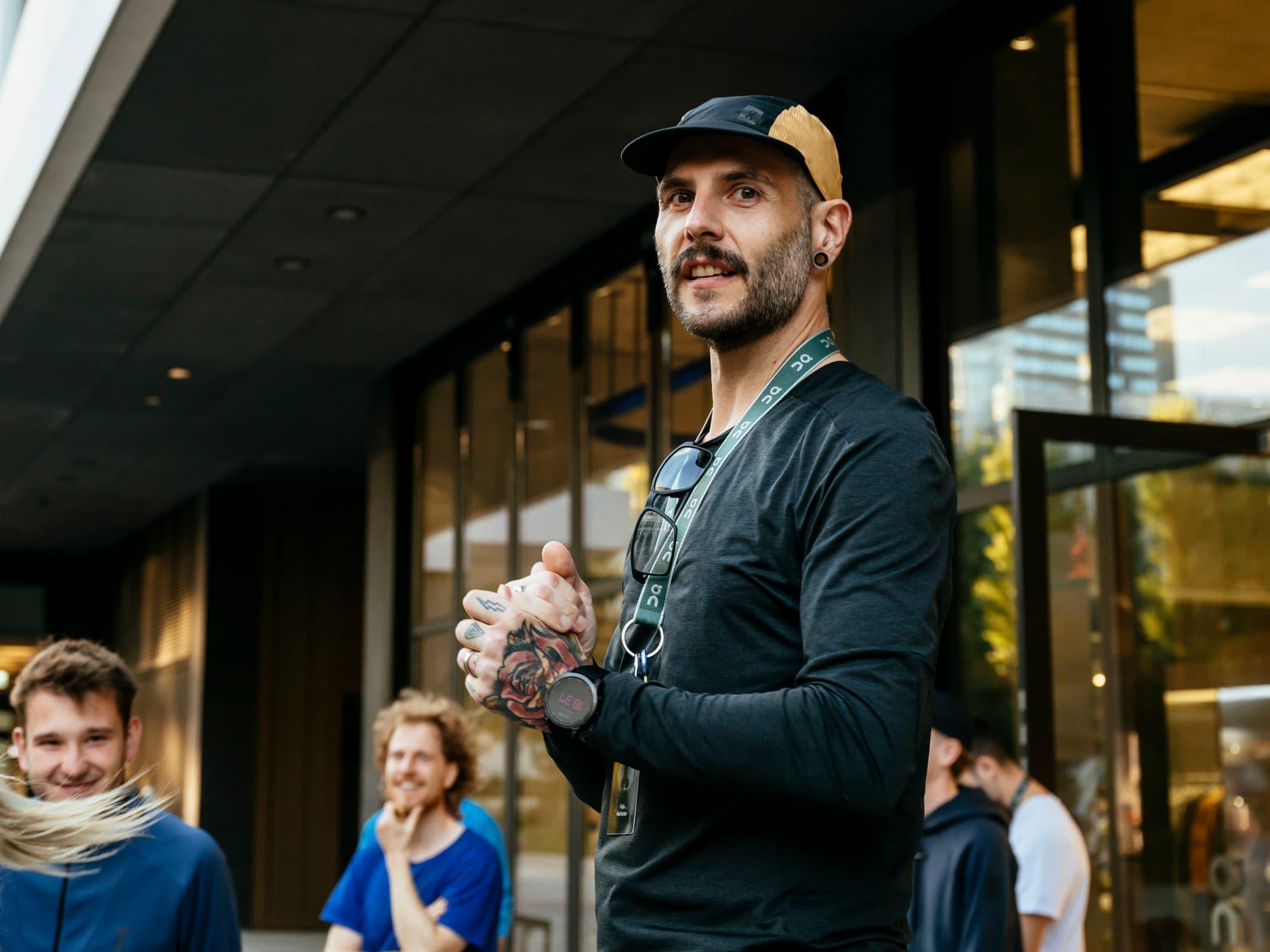 Man with tattooed hands in sportswear clapping his hands, with people around him