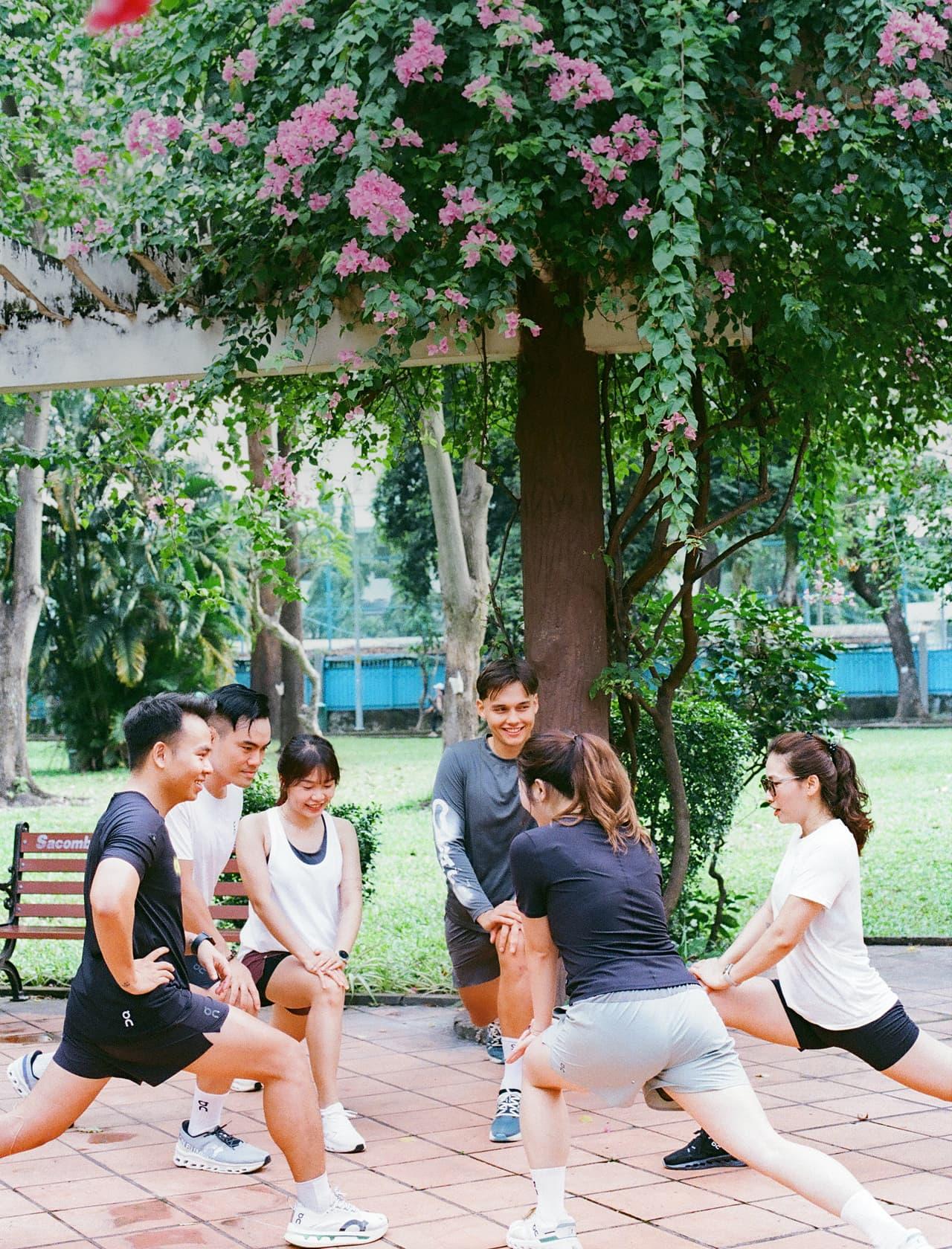 Two hands reach into a large shallow wooden bowl filled with bananas and green and red apples.