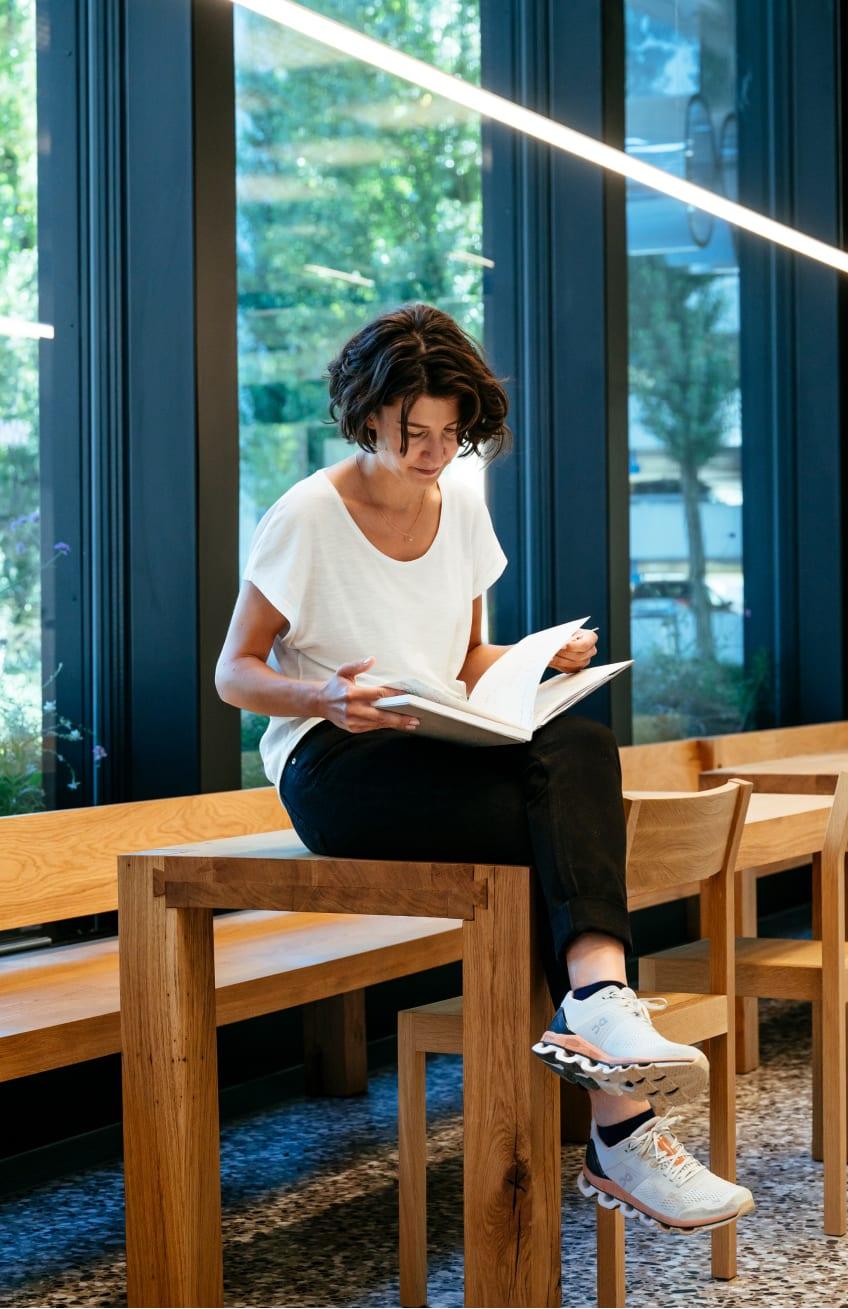 A woman sat on a wooden desk reading a book.