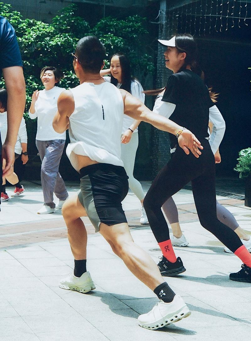 Group of people exercising outdoors on a sunny day, mid-motion in a dynamic stretching or warm-up activity.