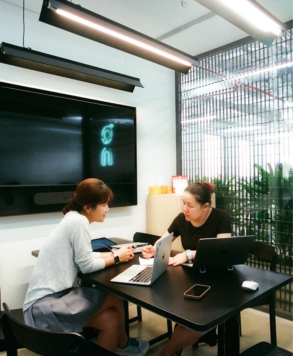 Two women sitting at a desk talking with two laptops