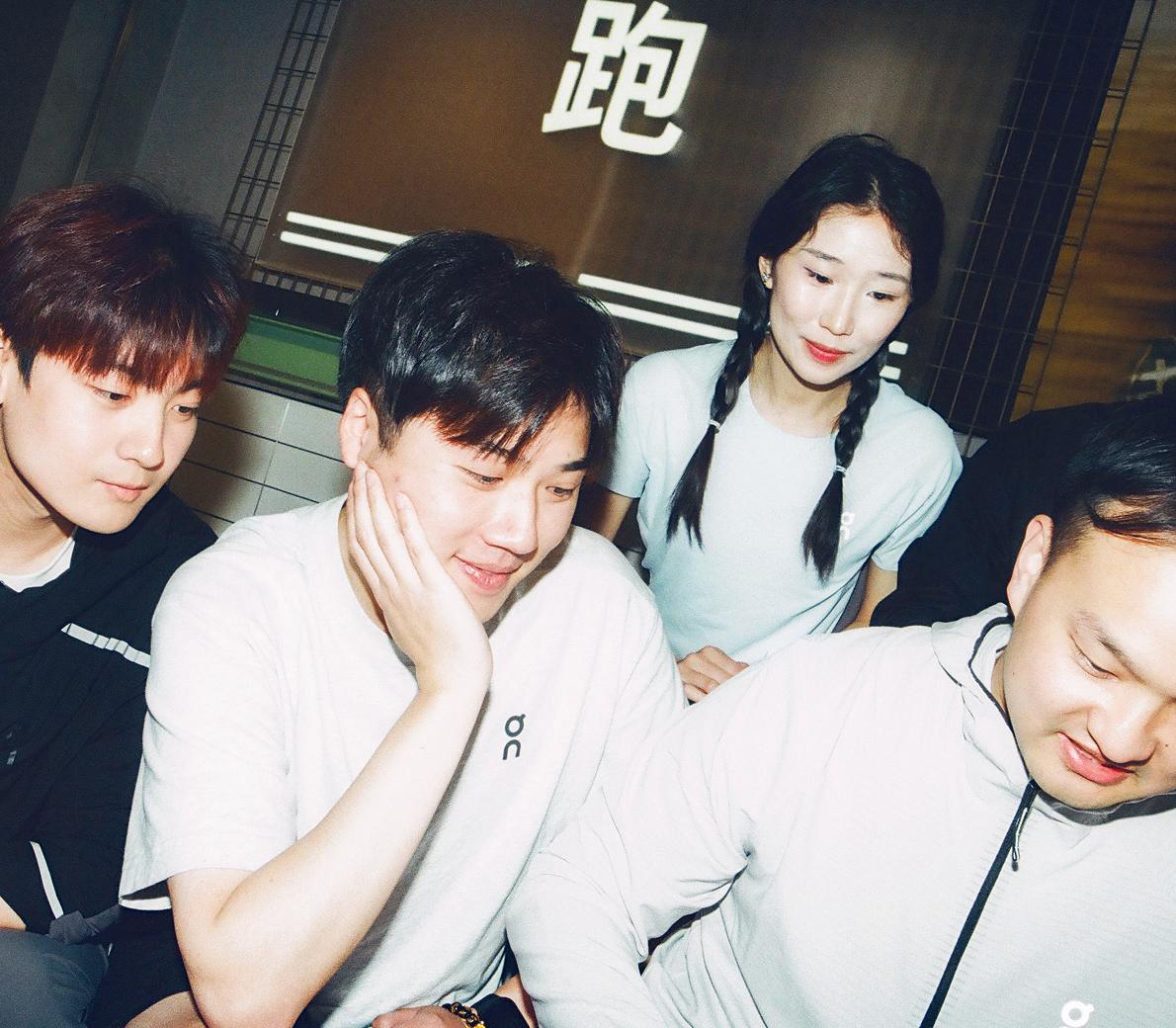 Group of four young adults gather closely around a screen, smiling and engaged.