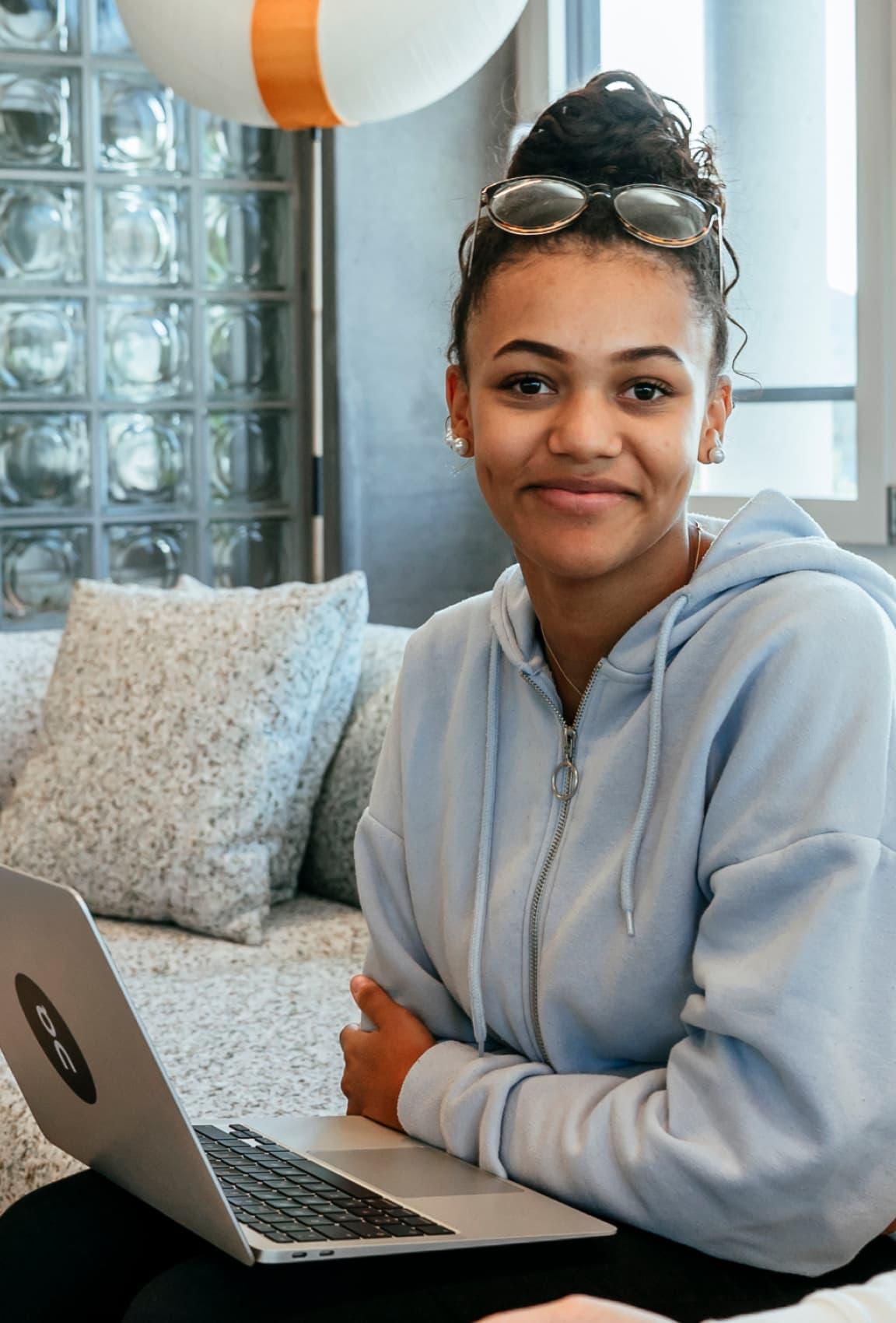 A young woman smiling at the camera, working on a laptop