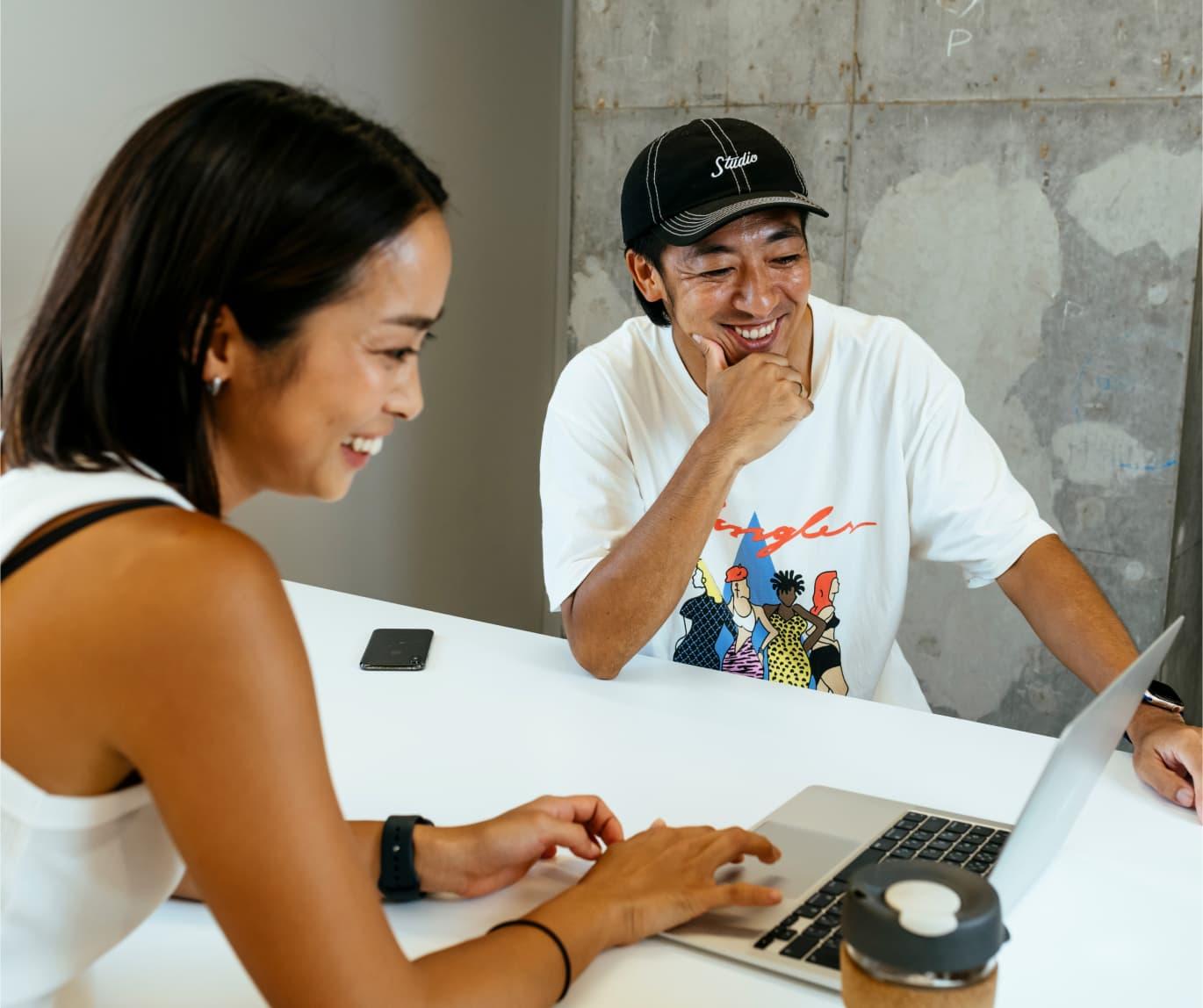 A woman and man smiling whilst looking at a laptop.