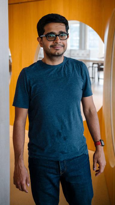 A man standing in a modern office looking at the camera, smiling slightly.