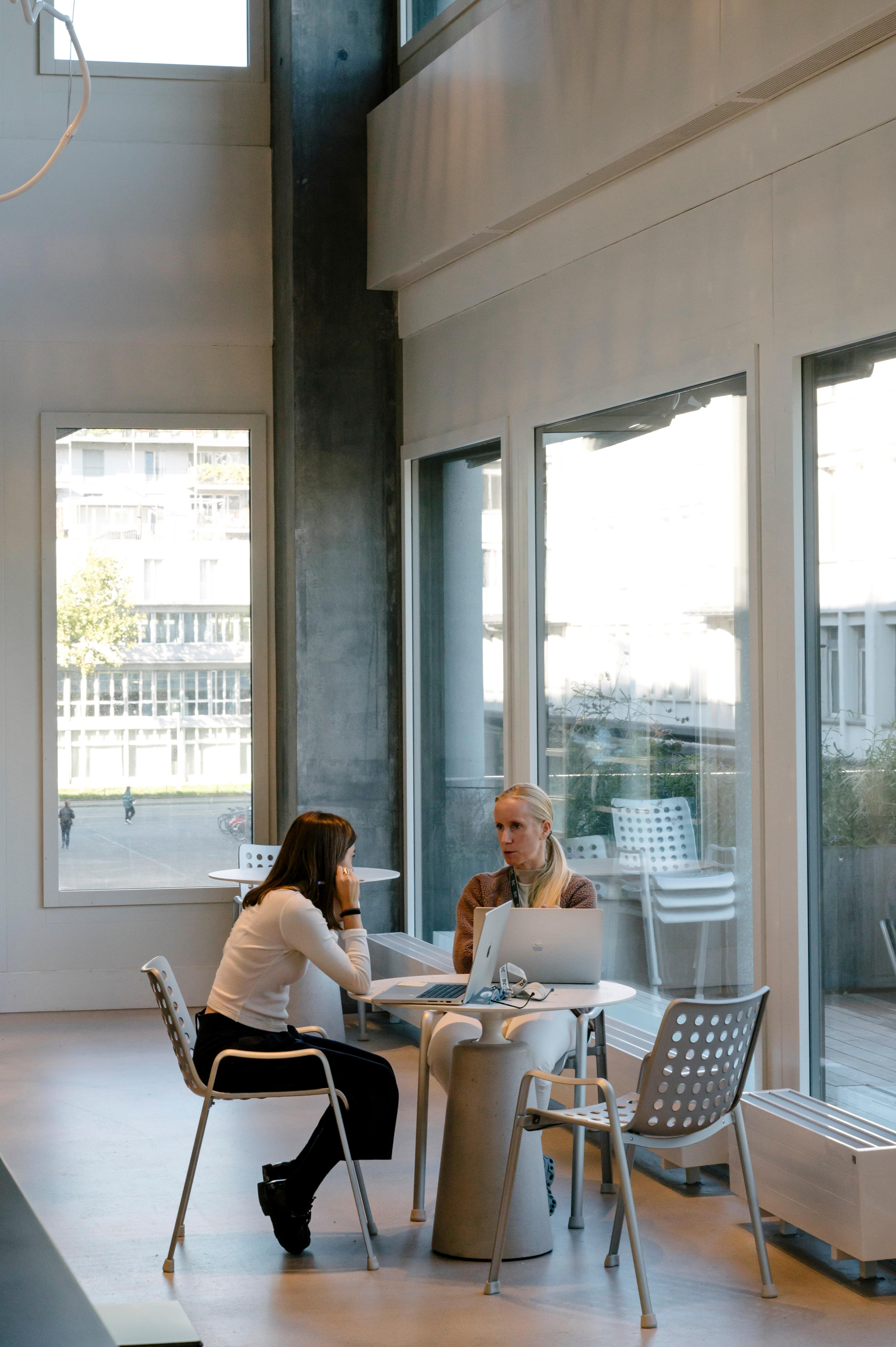 two women sitting at a table talking with laptops