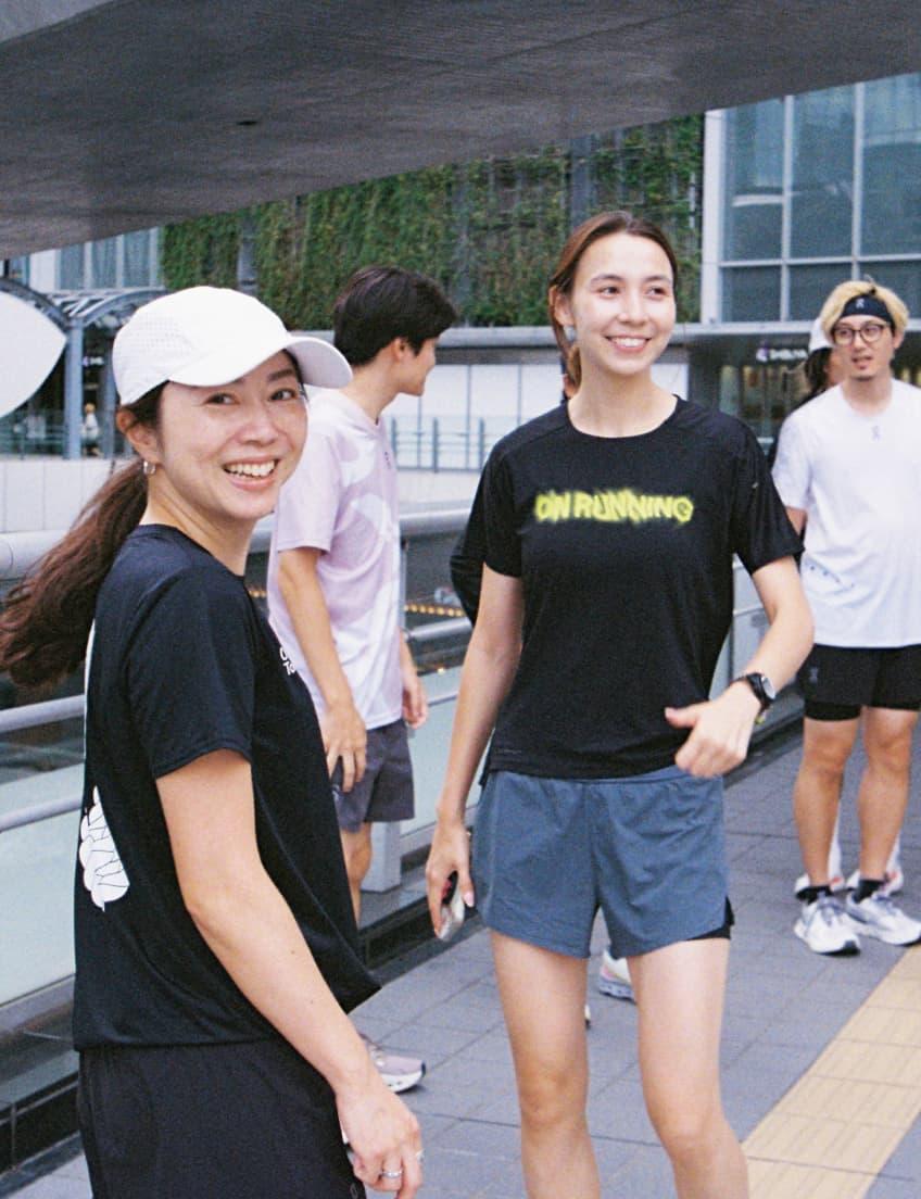 A small group of people in athletic clothing stand and smile on an outdoor walkway, with two women in the foreground.