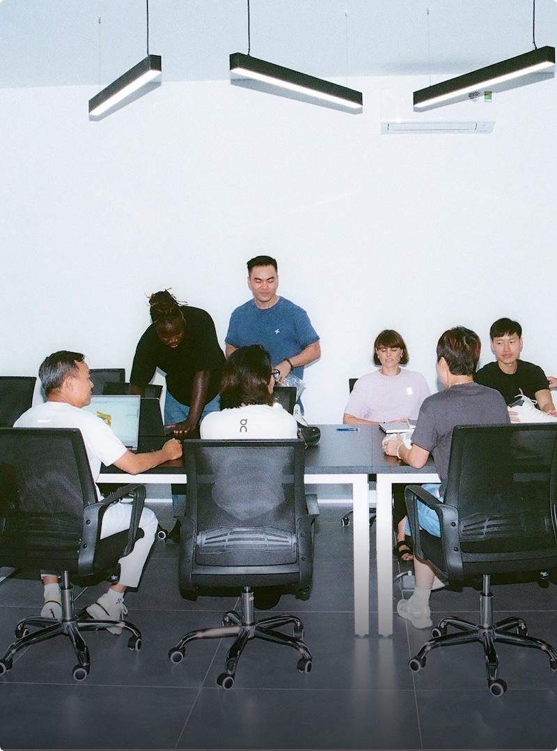 Eight people sit and stand around a conference table during a meeting in a minimalist office.