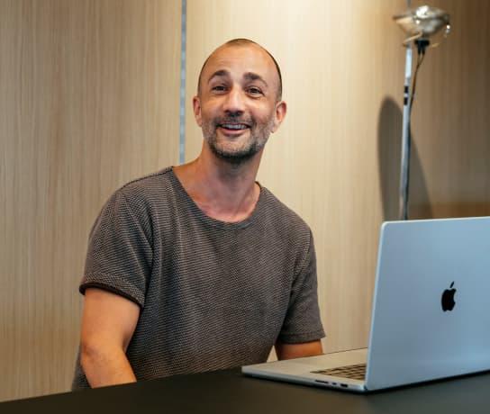 A man sat at a laptop smiling at the camera.