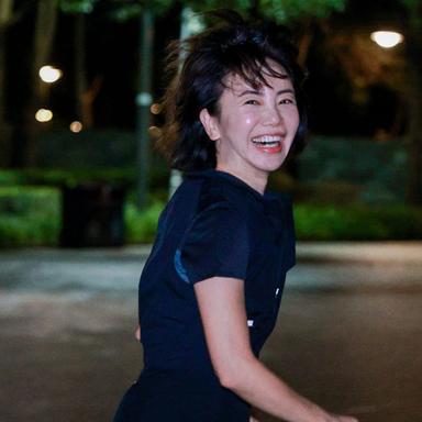 A woman running at night whilst smiling at the camera.