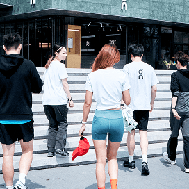 Five people in athletic clothing walk away from the camera toward steps leading into a modern building.