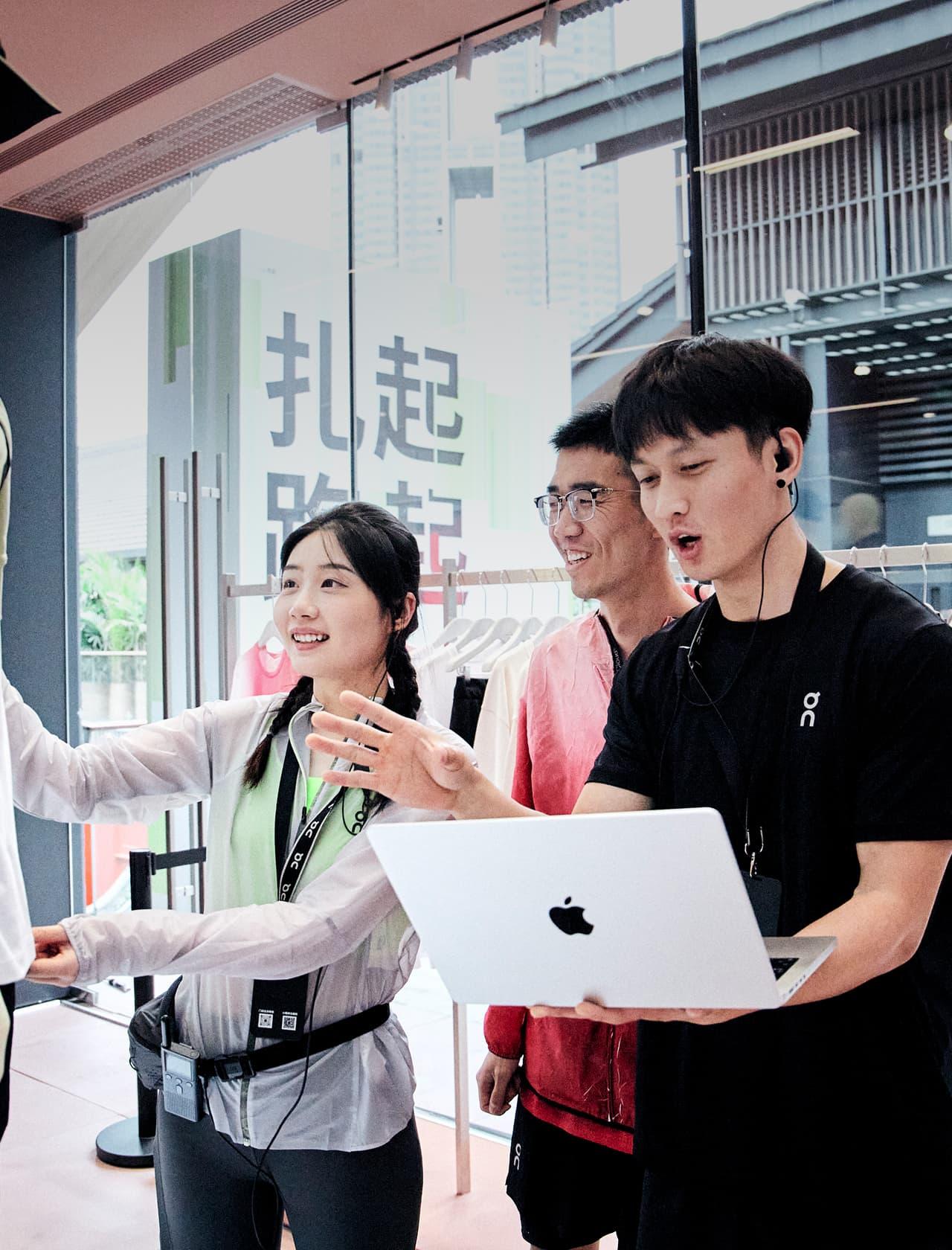 Three people in a clothing store are examining a garment while one person holds an open laptop.