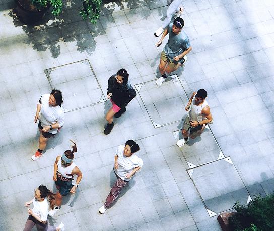 Overhead view of several people walking across a sunlit tiled outdoor plaza.