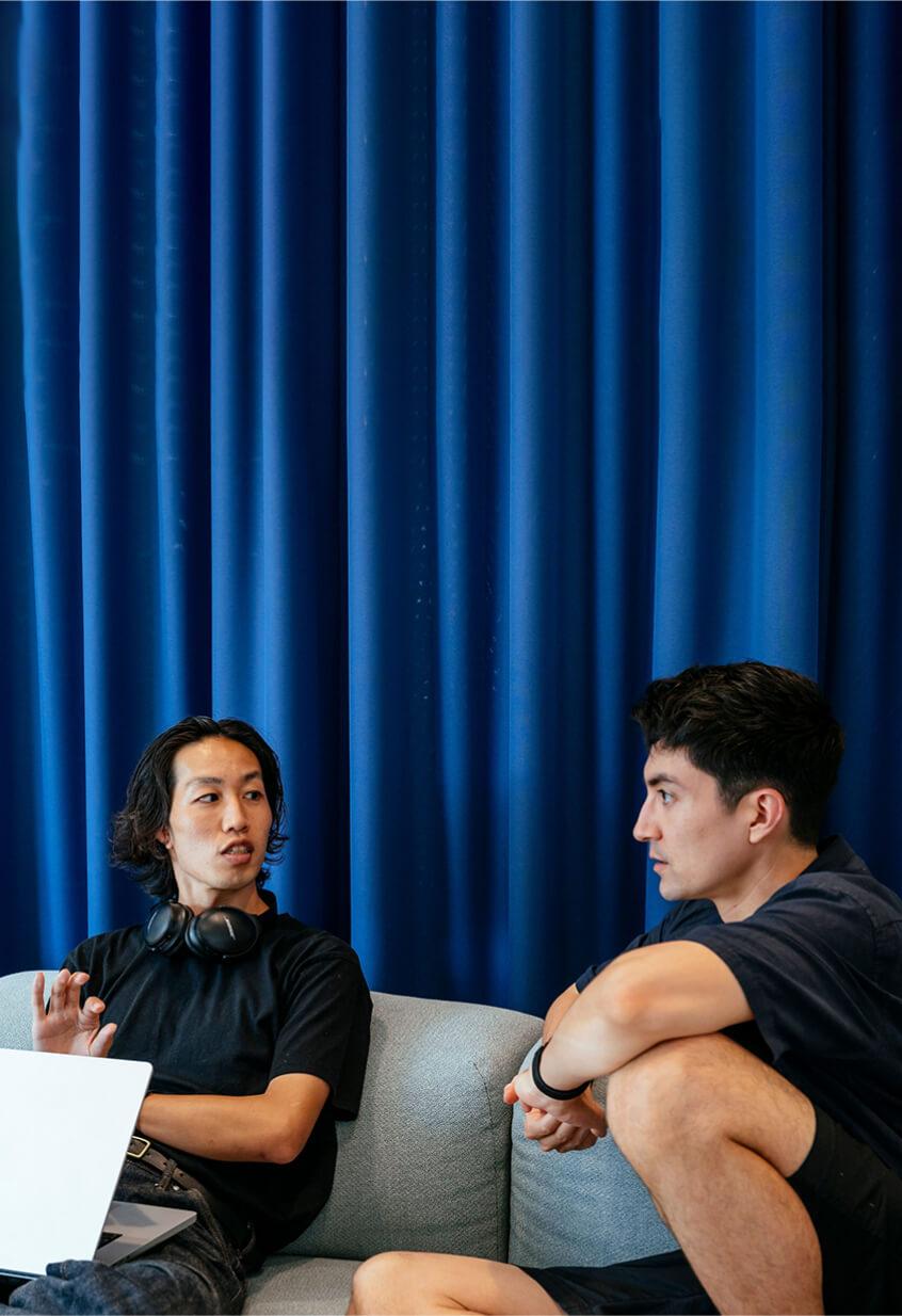 two men sitting discussing work infront of blue curtain