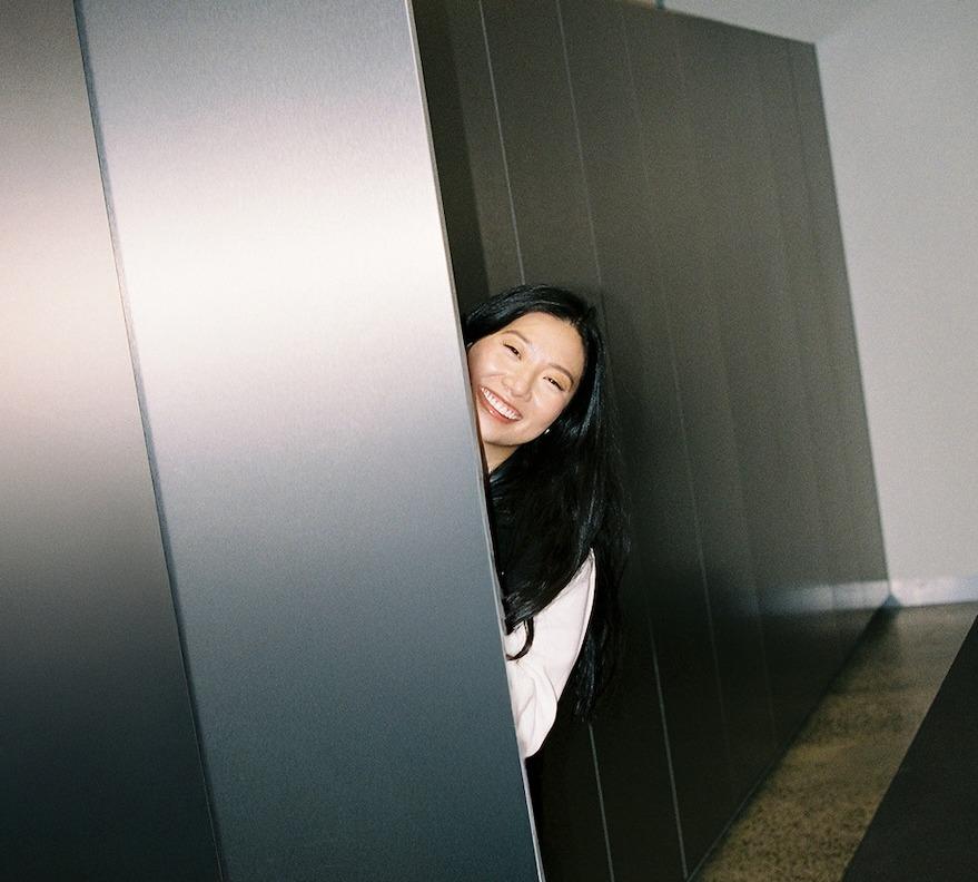 A smiling woman with long dark hair peeks around a tall gray metal partition.