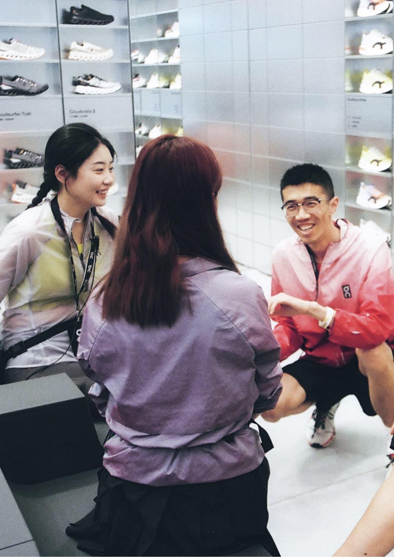 Five people talking and smiling inside a sneaker store, seated near shelves displaying On-brand athletic shoes.