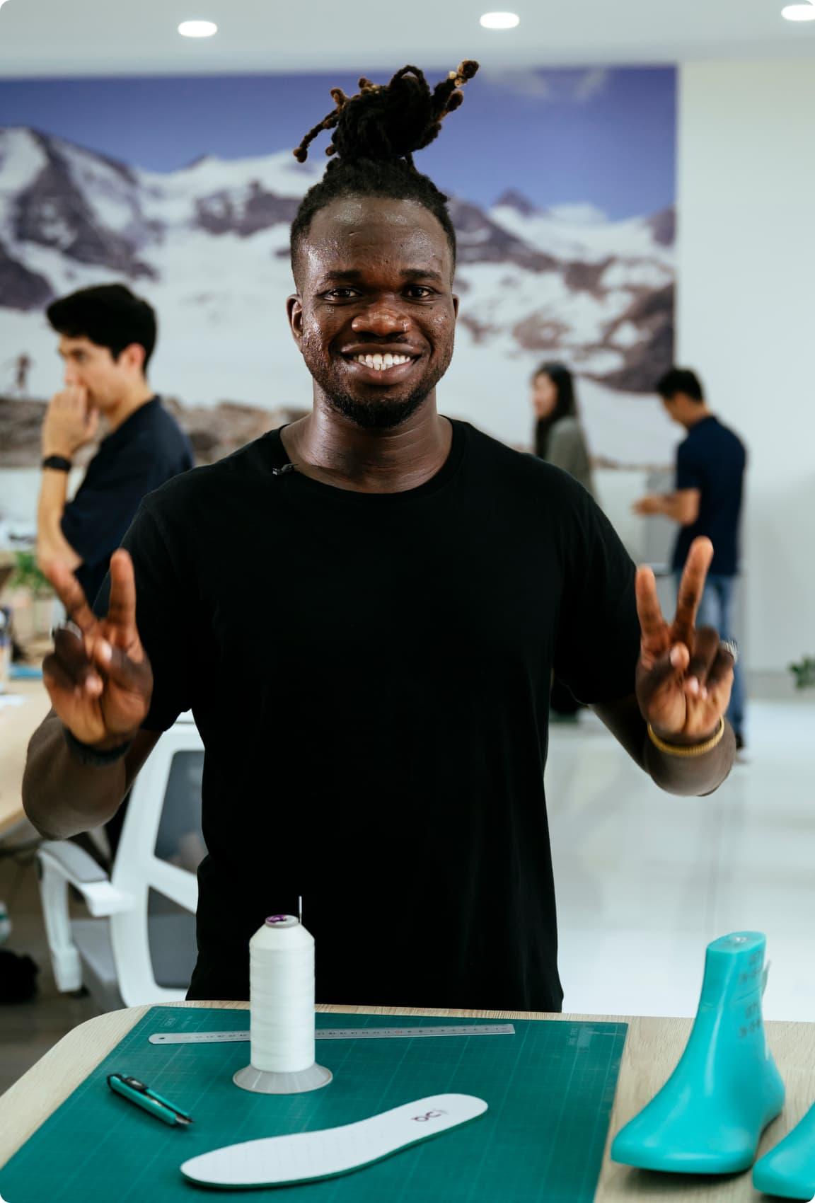 A man smiling to the camera whilst working on a shoe
