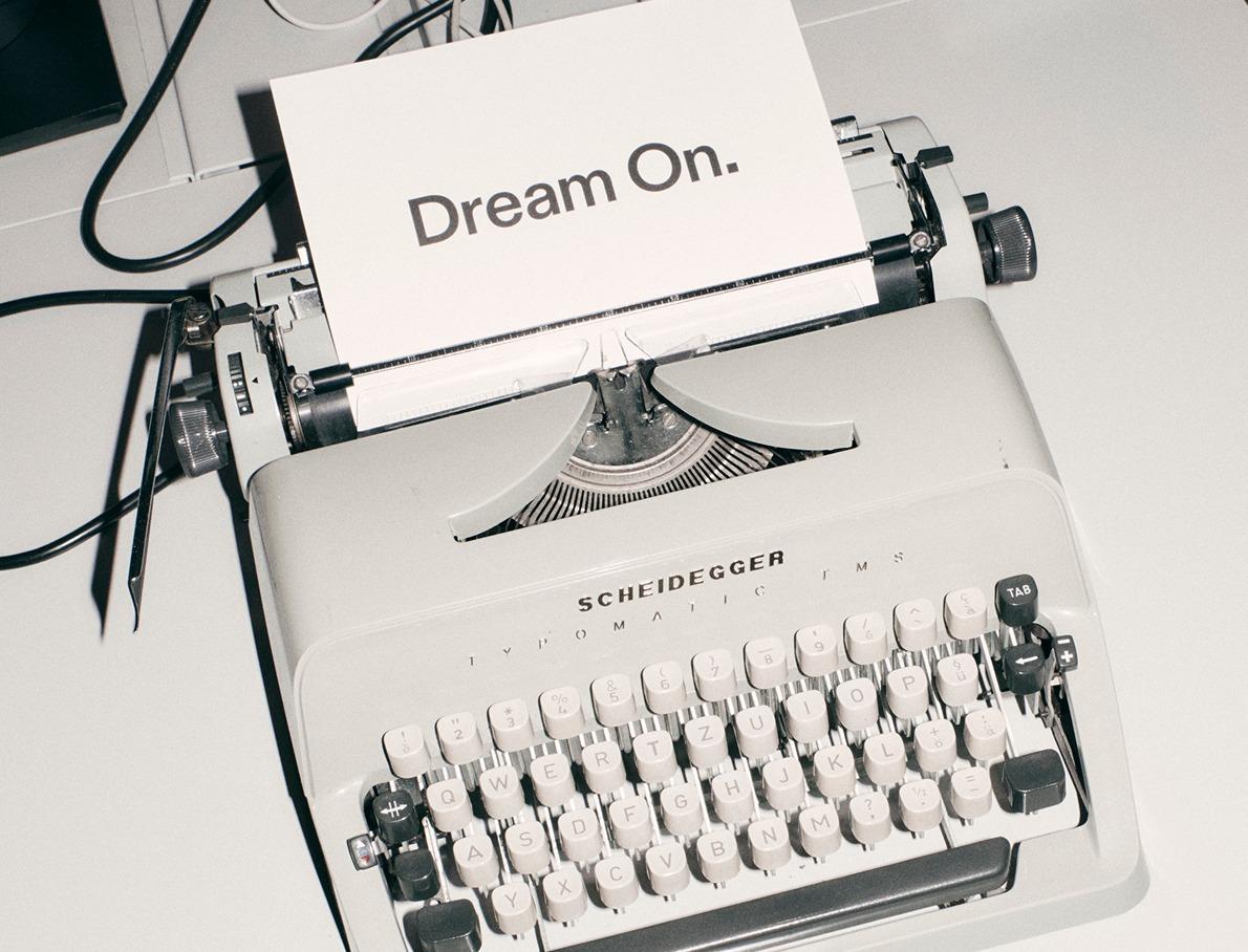 A vintage Scheidegger typewriter with a sheet of paper that reads “Dream On.”