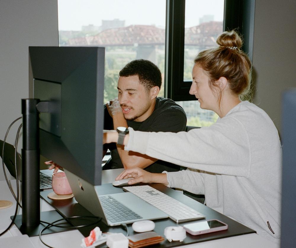 Two people working on laptops and desktop monitors are pointing towards a screen