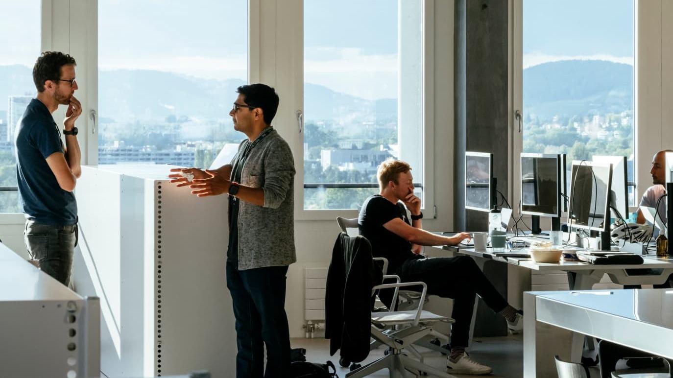 People stood up and sat down in an office with a view of the Swiss mountains outside the windows.