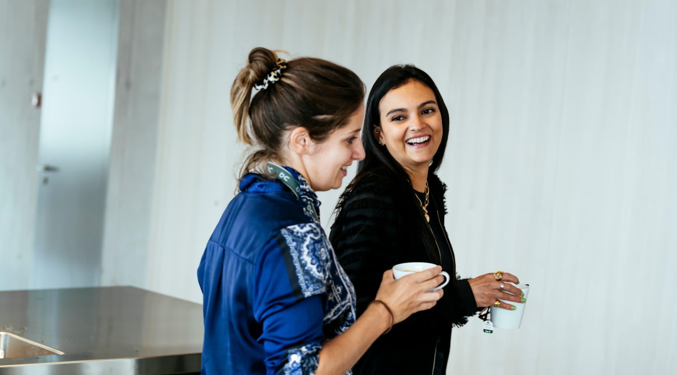 Two woman laughing whilst drinking from mugs