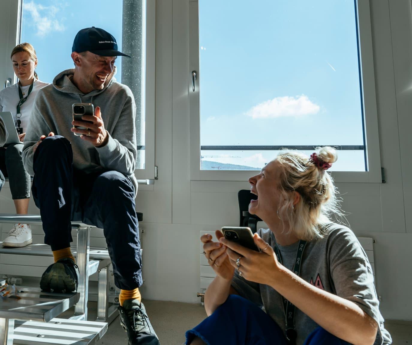 A man and woman laugh whilst looking at each other in a sun-filled room.
