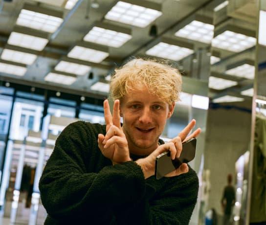 A man smiling at the camera gesturing peace signs with both hands.