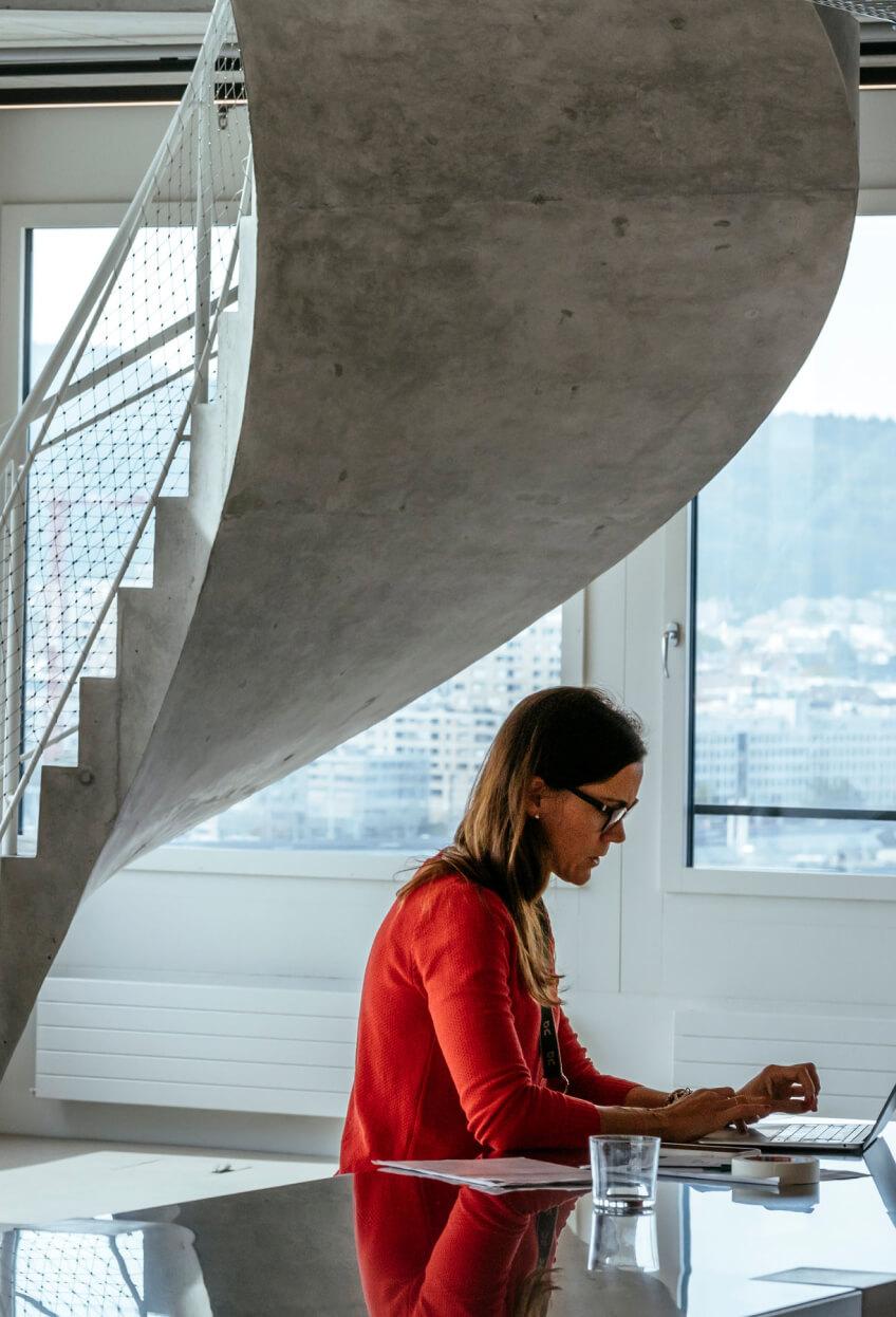 https:woman wearing red top working in modern concrete office