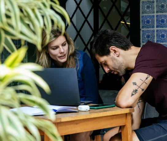 A man and a woman sitting at a table in a cafe, using a laptop