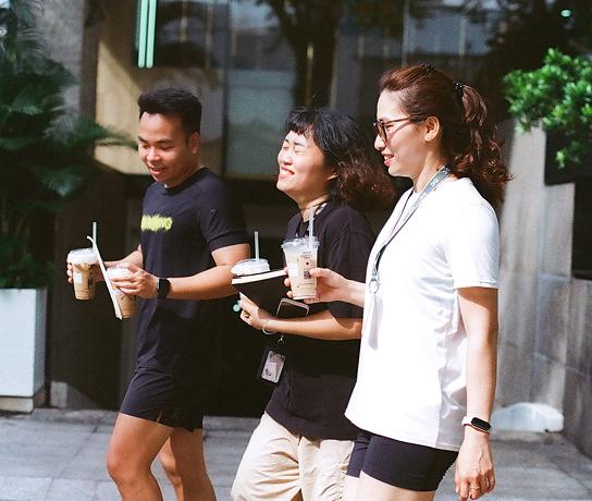 Three people walking outdoors, each holding an iced coffee and smiling.