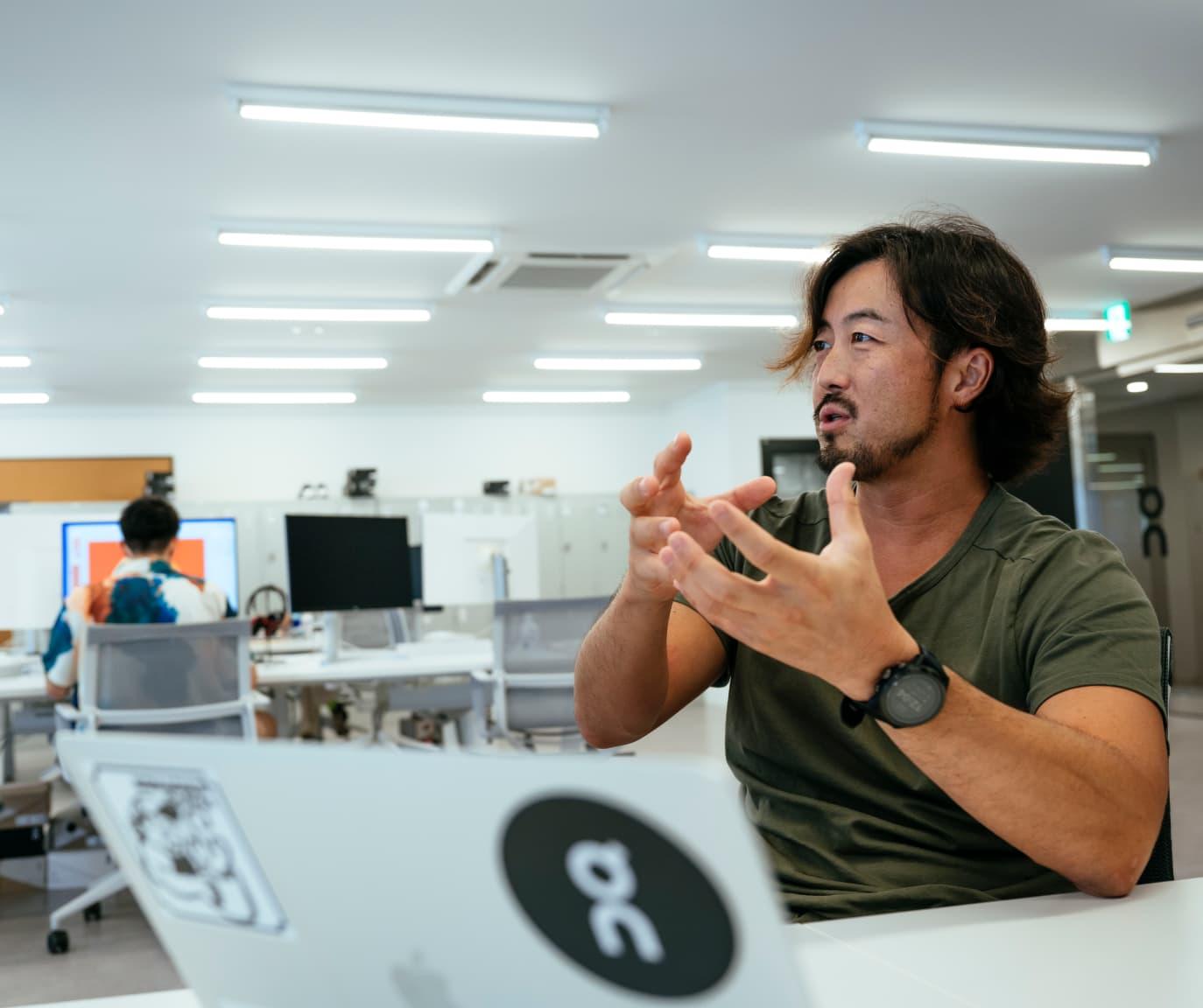 A man sat at his laptop talking whilst gesturing with his hands.