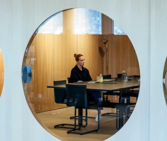A view through a circular office window of a woman working at a desk