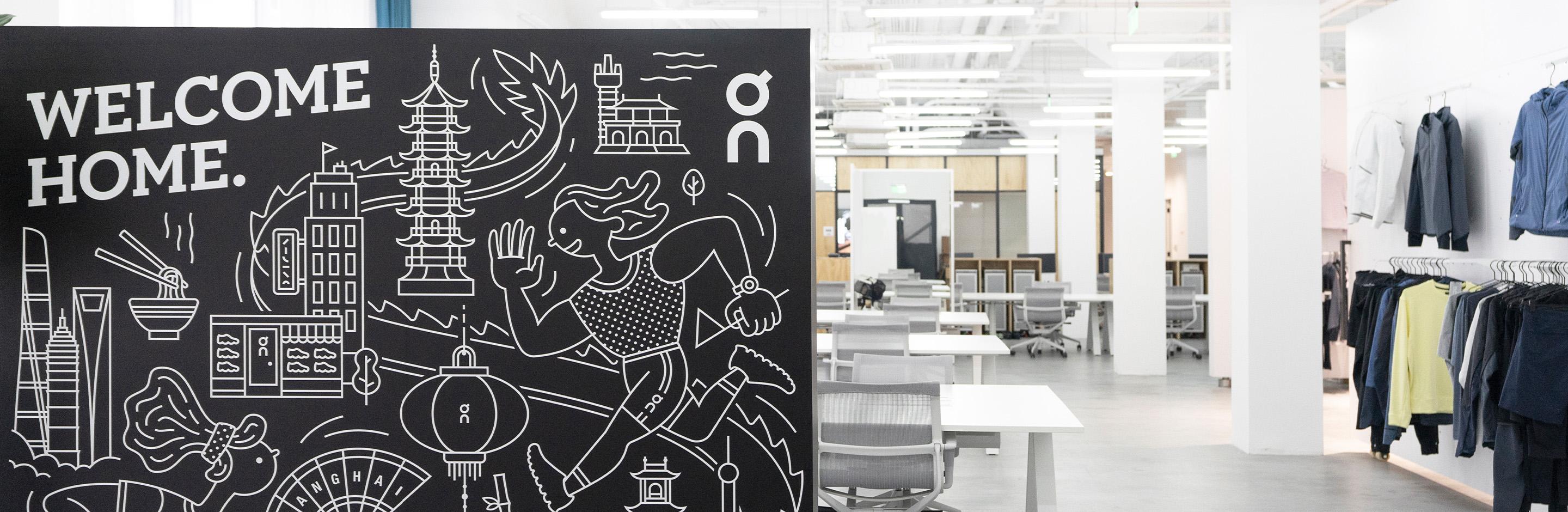 Split in half image: On the left is a Chalk board saying welcome home with a cartoon of a  running around Asian cultural references such as lanterns, noodles and buildings. The right hand side has an image of the empty office with apparel hung on the wall. 