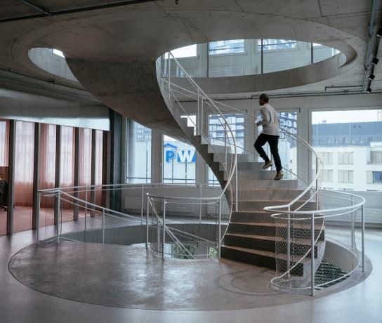 Man walking up a spiral concrete staircase in the Head Quarters of On Running