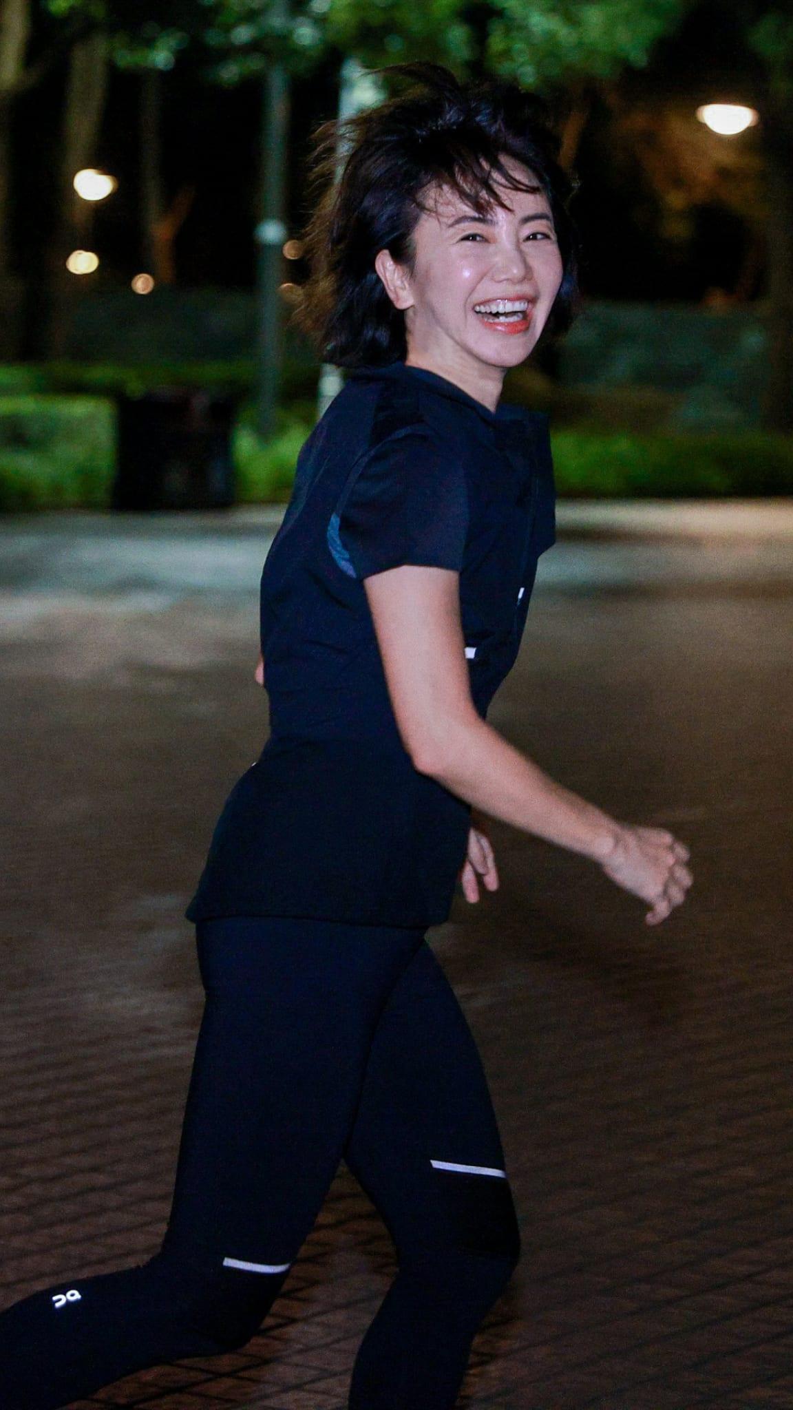 A woman running at night whilst smiling at the camera.