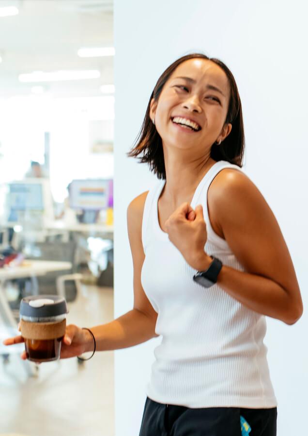 woman wearing onrunning sports clothes smiling and holding coffee