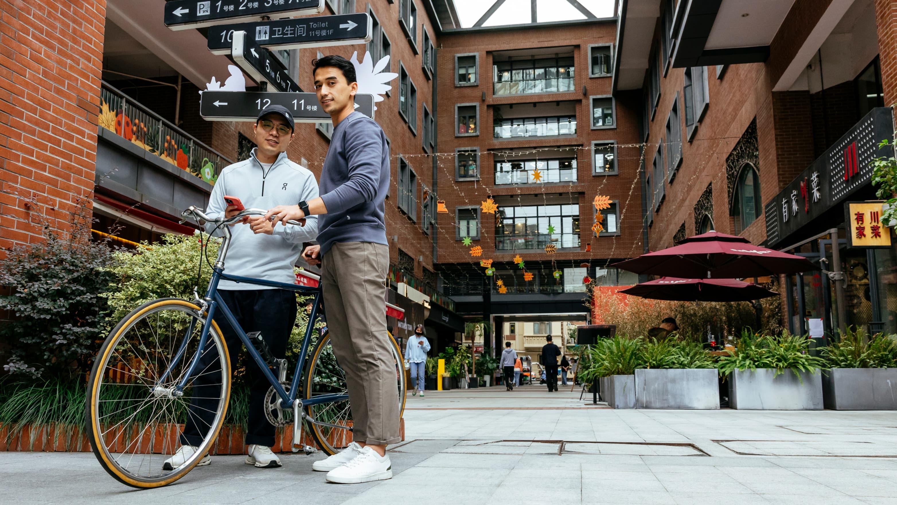 Two men stand and smile near the bicycle outside