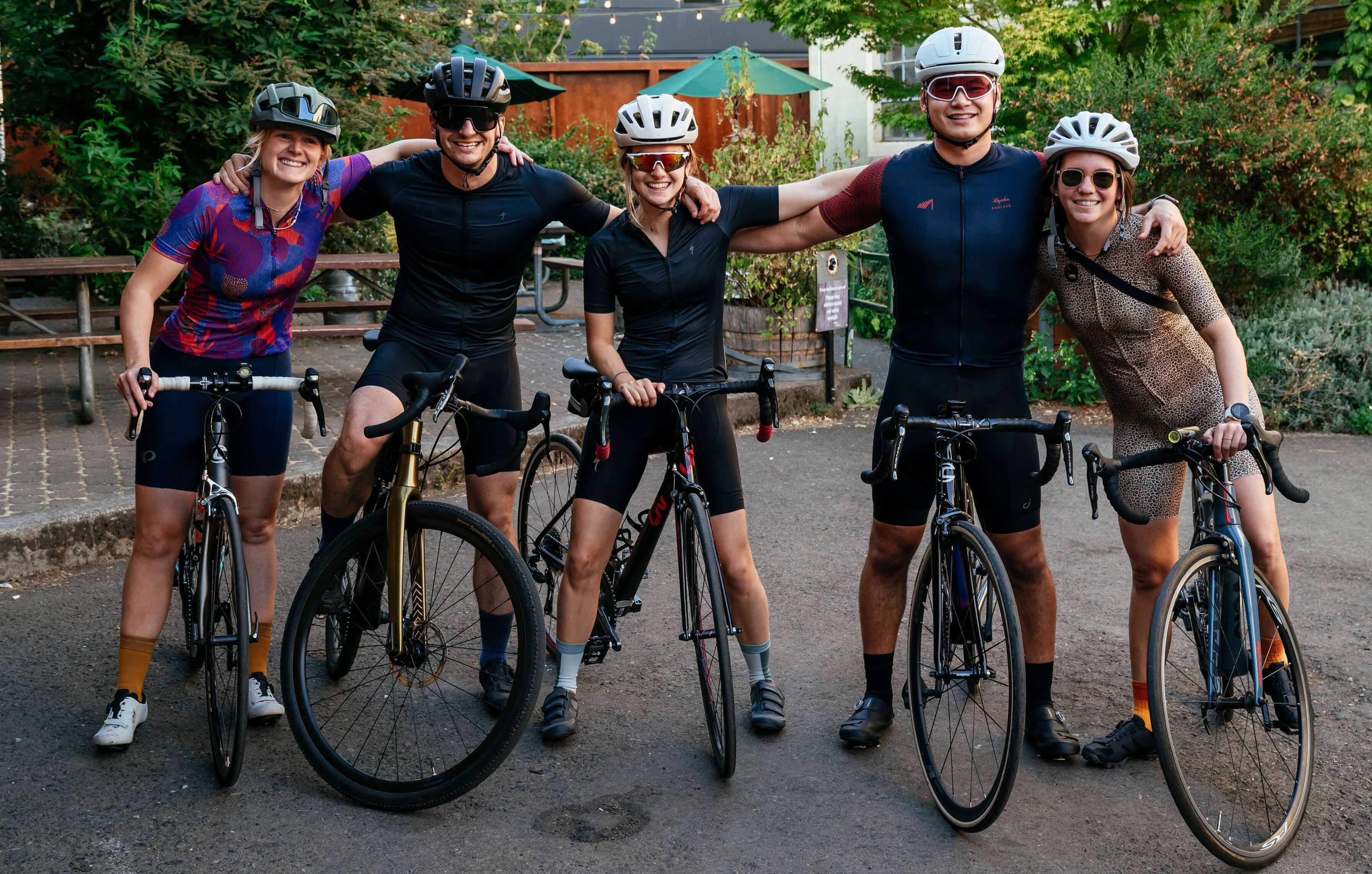 A group of cyclists on their bikes looking at the camera with their arms on each others shoulders