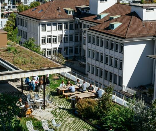 Aerial image of Zürich office rooftop garden with people sitting at benches on a sunny day.